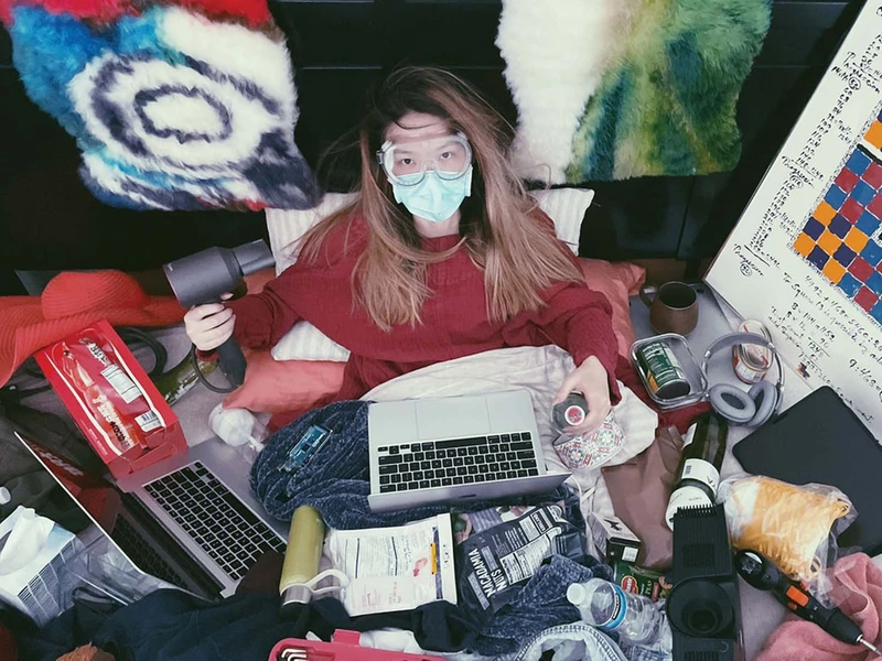 Photo of Dongpu Ling wearing goggles and a mask using a computer with various other items nearby