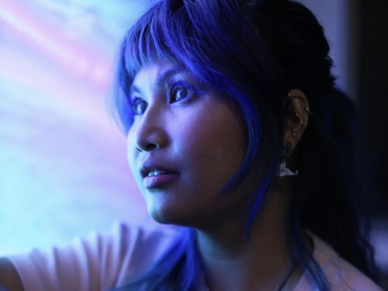 Photo of a person bathed in purple light, looking off camera.