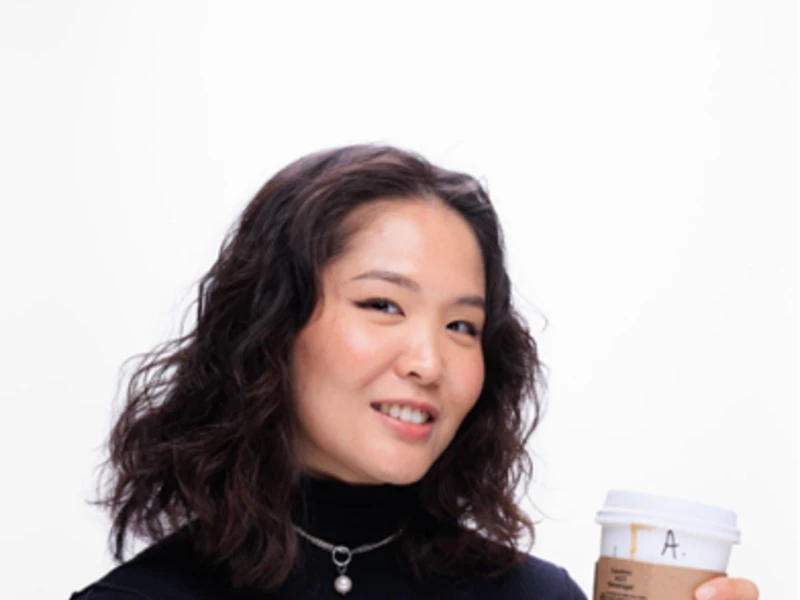 Person holding a coffee cup and smiling looks into the camera.